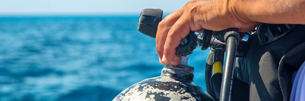 Scuba Diver Hand on Tank Closeup Closeup of the hand of a scuba diver on the nozzle of an oxygen tank on a boat with ocean water in background